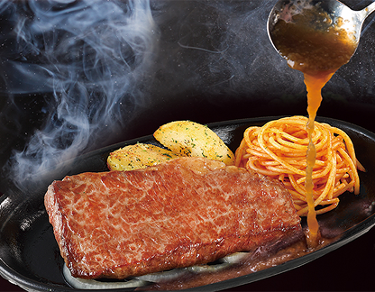 ステーキがのった熱々の鉄板にソースをかけている写真